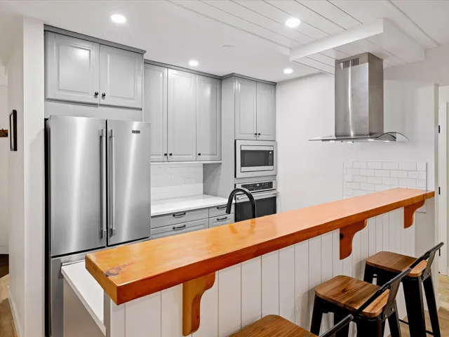 Kitchen with stainless steel appliances, wall chimney range hood, butcher block counters, decorative backsplash, and recessed lighting