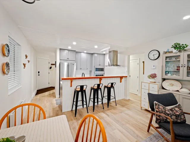 Kitchen featuring island range hood, stainless steel microwave, a peninsula, light wood finished floors, and a kitchen breakfast bar