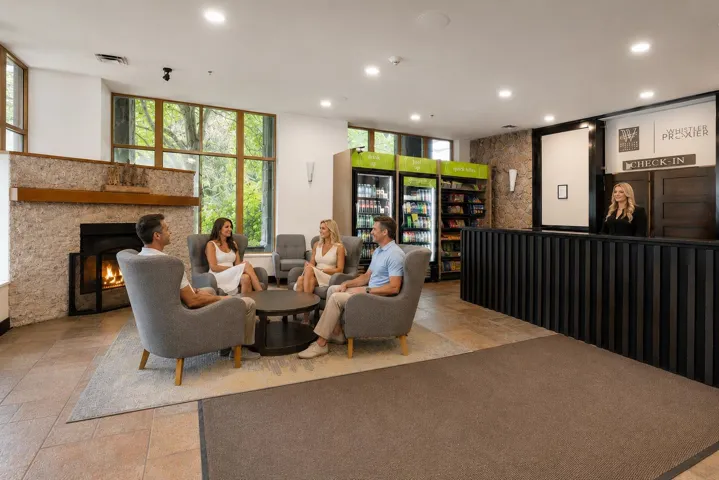 Spacious lobby area featuring a stone-clad fireplace with a wood mantel, large multi-pane windows, and a check-in desk with a textured facade