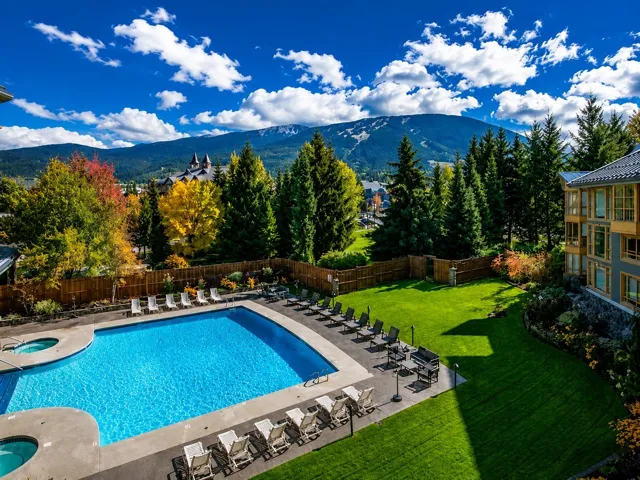 Outdoor swimming pool and two integrated hot tubs surrounded by a concrete deck, manicured lawn, and mature trees