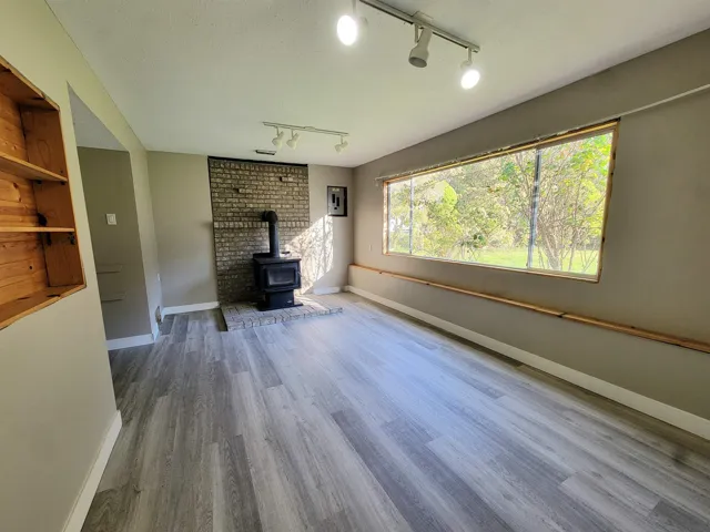 Unfurnished living room with a wood stove, rail lighting, light wood finished floors, and plenty of natural light