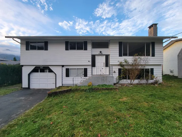 Bi-level home featuring a front lawn, a garage, asphalt driveway, and a chimney