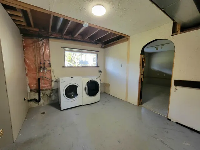 Laundry area with arched walkways, concrete floors, washing machine and clothes dryer, and a textured ceiling