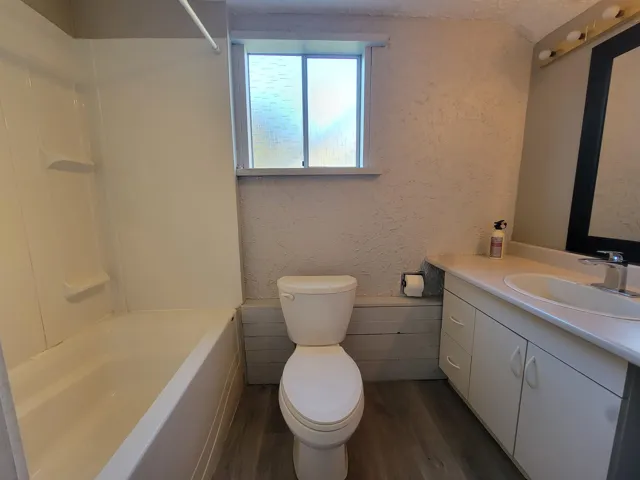 Bathroom with a textured wall, dark wood-type flooring, vanity, and shower / bath combination