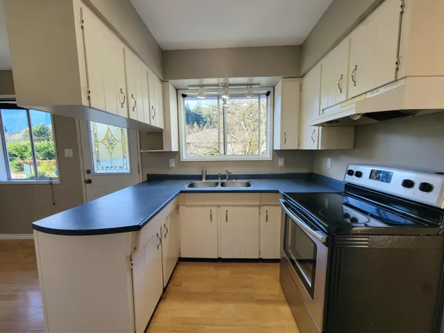 Kitchen with stainless steel range with electric stovetop, under cabinet range hood, dark countertops, light wood finished floors, and a peninsula