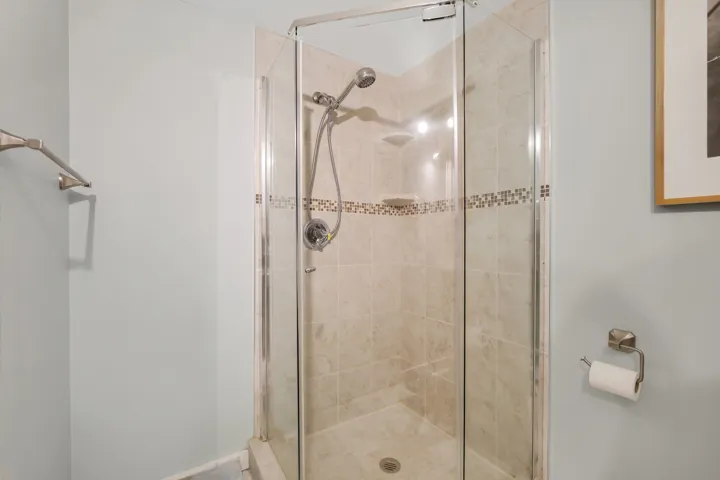 Enclosed shower featuring tile surround, mosaic accent band, and a glass door