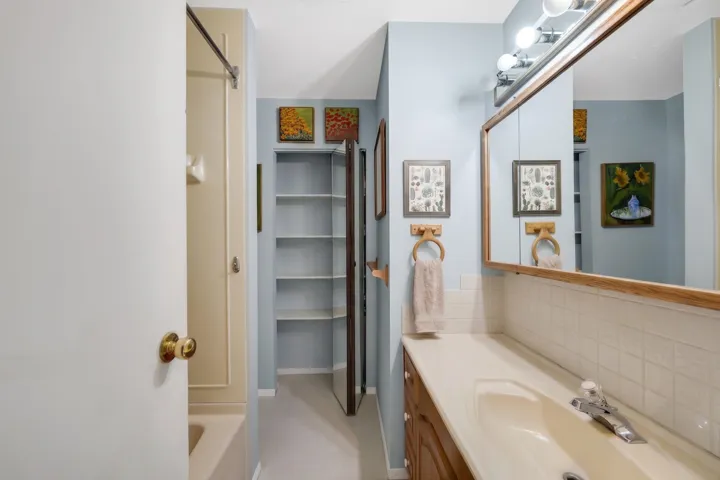 Bathroom featuring a light blue wall color, wood-finish vanity with an integrated sink, and a large mirrored medicine cabinet with overhead lighting