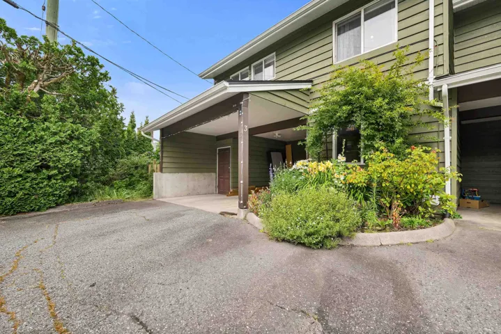 Exterior featuring a covered carport, green siding, multiple windows, established trees, and a garden bed