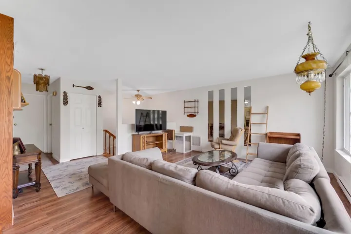 Spacious living area featuring wood-finish flooring, white walls, and a large window providing natural light