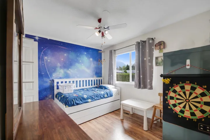Bedroom featuring a vibrant accent wall, wood-finish flooring, and a ceiling fan