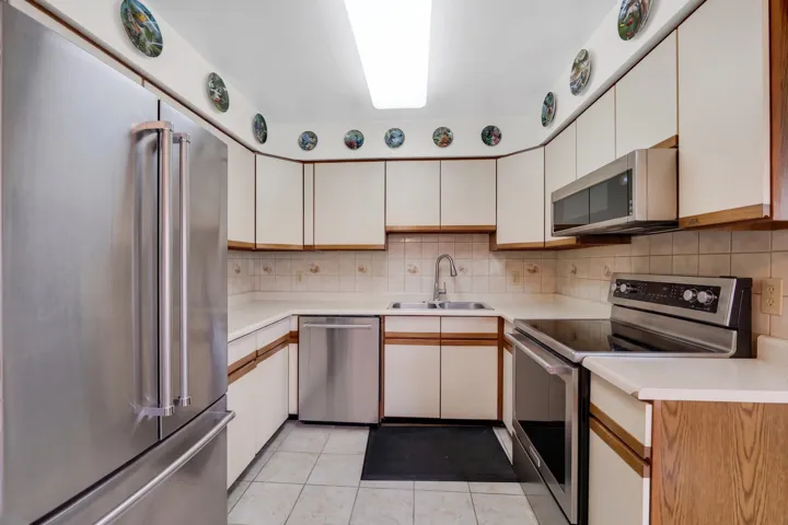 Kitchen featuring stainless steel appliances, white cabinetry with wood trim, and light-toned countertops