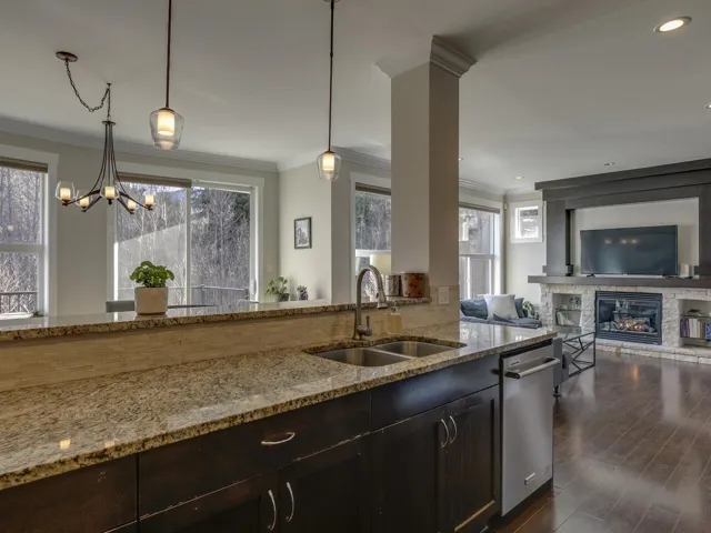 Kitchen with light stone counters, hanging light fixtures, crown molding, a stone fireplace, and open floor plan