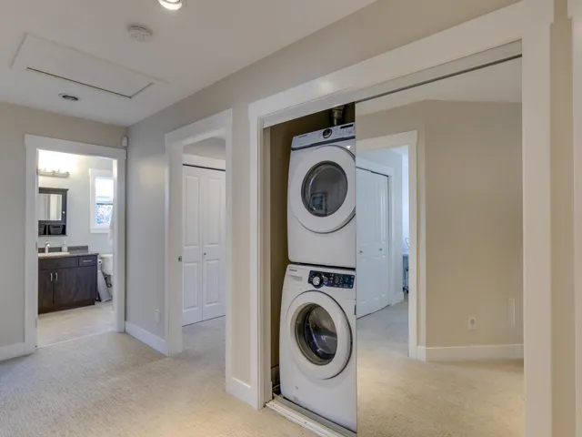 Washroom with light colored carpet and stacked washer / drying machine