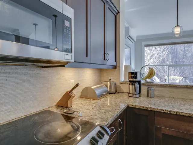 Kitchen featuring stainless steel microwave, black electric stovetop, light stone countertops, and a wall unit AC