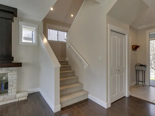 Stairs with plenty of natural light, crown molding, wood finished floors, a stone fireplace, and recessed lighting