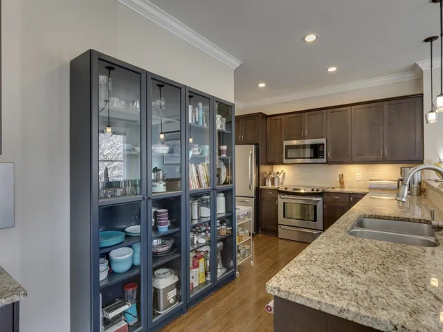 Kitchen featuring light stone countertops, dark brown cabinets, stainless steel appliances, hanging light fixtures, and crown molding