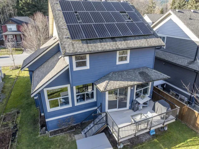 Rear view of house with roof with shingles, a wooden deck, a yard, and solar panels
