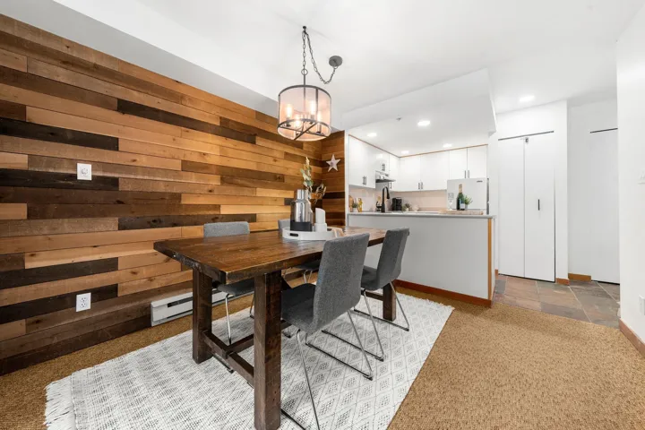 Dining area featuring a wood plank accent wall, a chandelier with an exposed bulb design, and a solid wood dining table