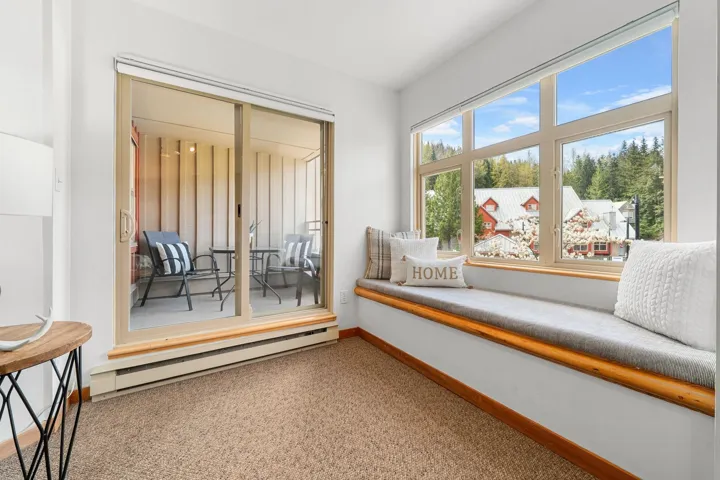 Sunlit room featuring a built-in window seat with a cushioned top, expansive multi-pane window, and a sliding glass door opening to a private balcony