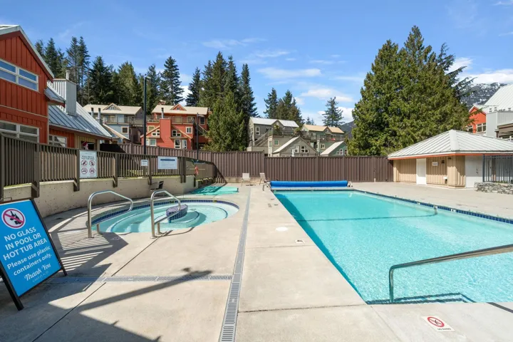 Outdoor swimming pool and hot tub area featuring concrete decking, metal handrails, and surrounding privacy fencing