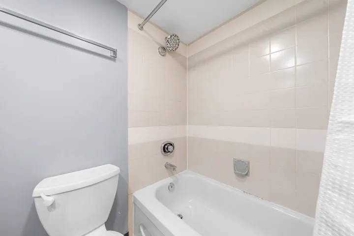 Tub and shower combination featuring tiled walls, a rain shower head, and chrome fixtures