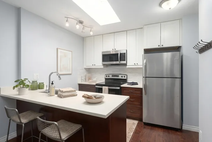 Kitchen featuring a breakfast bar with seating, stainless steel appliances, a tile backsplash, two-tone cabinetry, and a skylight