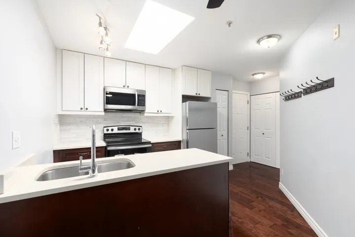Contemporary kitchen featuring a skylight, white upper cabinetry, dark wood-finish lower cabinetry, and stainless steel appliances