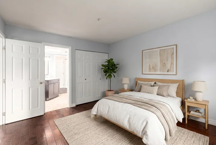 Spacious room featuring rich wood-finish flooring, light blue wall tones, and white bi-fold closet doors