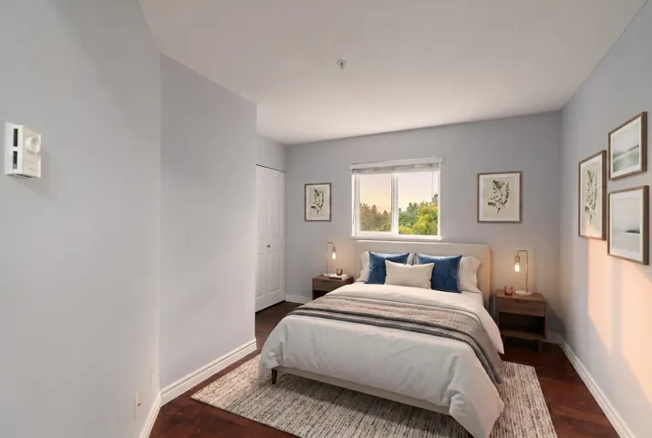 Room featuring wood-finish flooring, light grey painted walls, a window with a white frame, and a white bi-fold closet door