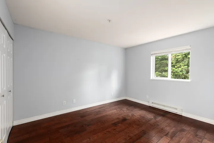 Primary bedroom with window and hardwood flooring