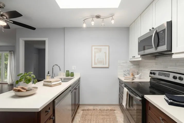 Modern kitchen with white countertops, stainless steel appliances, white upper cabinetry, and dark wood-finish lower cabinetry
