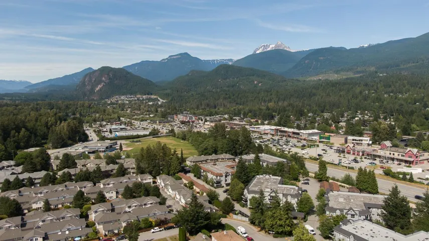 Mountainous backdrop with a forested landscape, featuring residential developments, commercial establishments, and a visible roadway