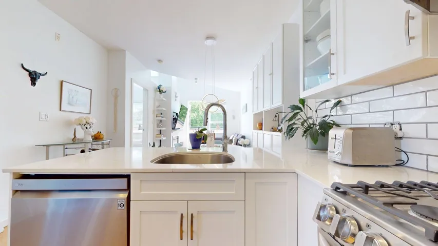 Kitchen featuring a peninsula, stainless steel appliances, white cabinetry, decorative backsplash, and glass insert cabinets