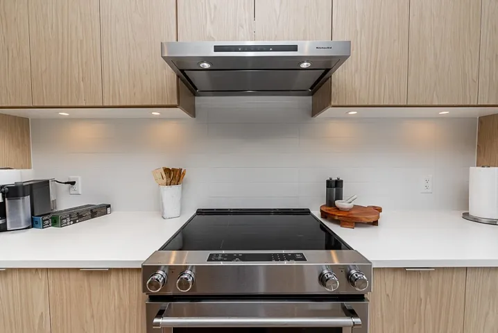 Kitchen with extractor fan, stainless steel range with electric stovetop, decorative backsplash, and light brown cabinetry
