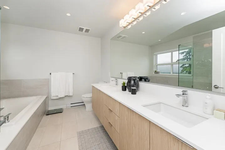 Bathroom featuring a baseboard radiator, double vanity, a bath, tile patterned flooring, and toilet