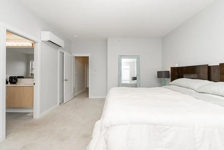 Bedroom featuring a wall mounted air conditioner, light colored carpet, ensuite bath, and baseboards