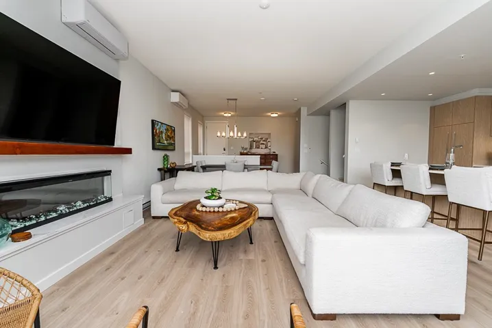 Living area featuring a wall mounted AC, light wood-type flooring, a glass covered fireplace, and a chandelier