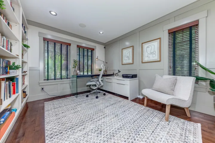 Dedicated office space featuring rich wood-finish flooring, recessed lighting, and extensive built-in shelving