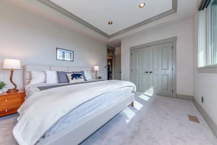 Spacious bedroom featuring light gray carpeting, a tray ceiling with recessed lighting, and a large window providing natural light
