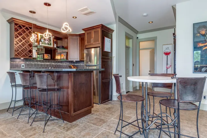Built-in bar featuring dark wood cabinetry, integrated wine storage, a dark tile backsplash, and a polished stone countertop