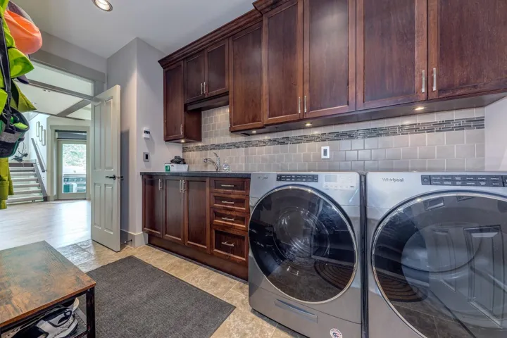 Dedicated laundry area featuring dark wood-finish cabinetry, a sink, and a tiled backsplash with decorative accent