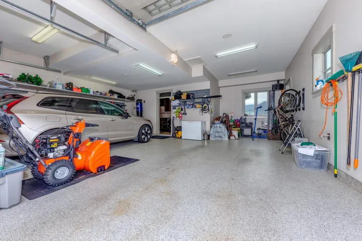 Spacious garage featuring an epoxy-coated concrete floor, overhead fluorescent lighting, and integrated wall shelving for organized storage