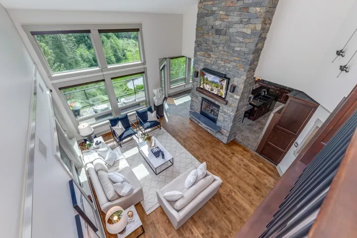 Spacious living area featuring large windows, a floor-to-ceiling stone fireplace, high ceilings, and wood-finish flooring