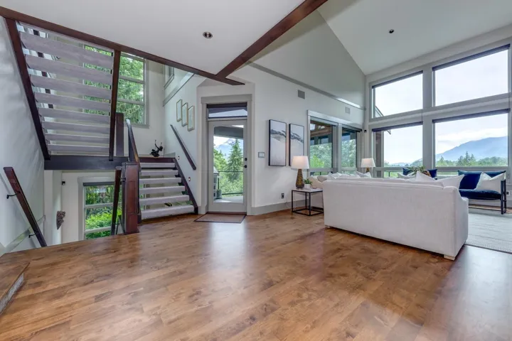Open-concept living space with wood-finish flooring, a contemporary staircase, and a wall of windows