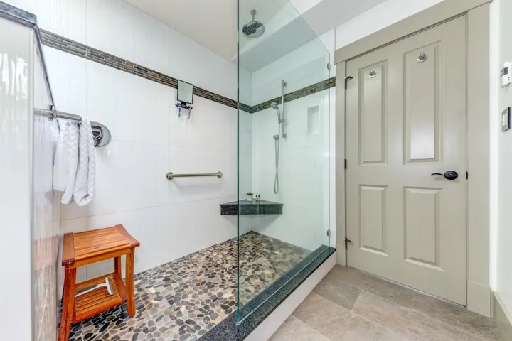 Spacious shower featuring pebble tile flooring, glass enclosure, and a built-in corner bench