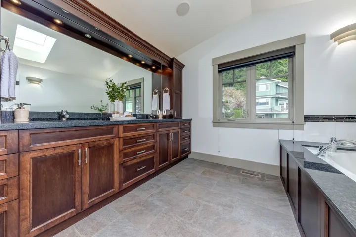 Double vanity with dark wood cabinetry and granite countertops, featuring dual sinks and an expansive mirror with integrated lighting