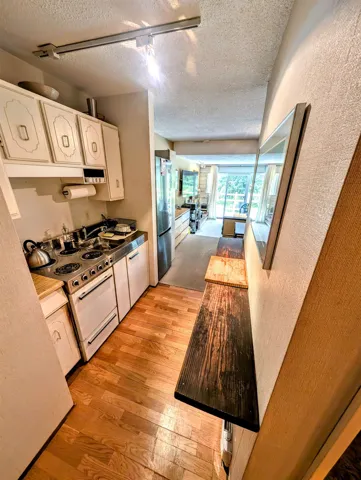 Kitchen with white cabinetry, light wood-style flooring, electric range oven, a textured wall, and a textured ceiling
