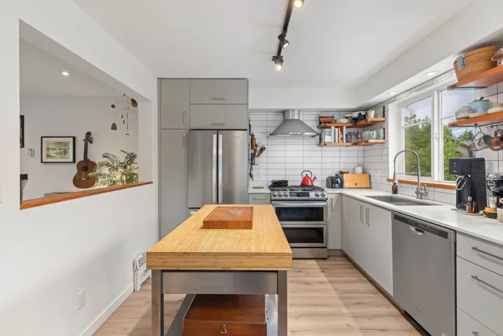 Kitchen featuring stainless steel appliances, gray cabinets, open shelves, wall chimney range hood, and tasteful backsplash