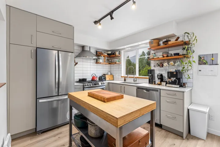 Kitchen featuring appliances with stainless steel finishes, gray cabinetry, open shelves, and wall chimney exhaust hood