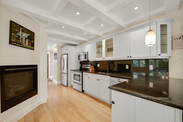 Kitchen featuring glass insert cabinets, stainless steel appliances, white cabinetry, recessed lighting, and beamed ceiling